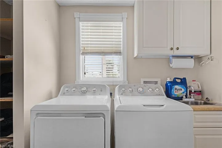 Clothes washing area with sink, cabinets, and washer and dryer