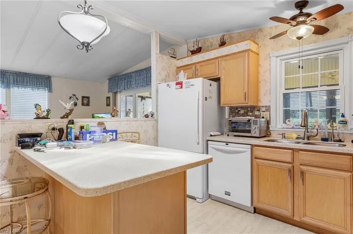 Kitchen with lofted ceiling, white appliances, backsplash, hanging light fixtures, and sink