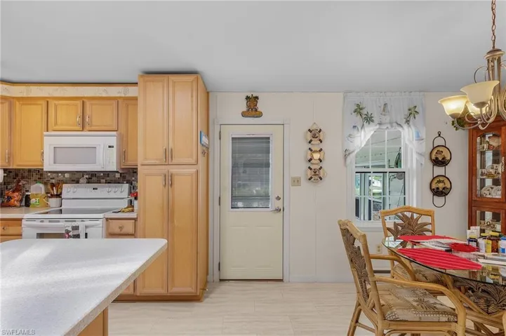 Kitchen with white appliances, pendant lighting, light brown cabinets, decorative backsplash, and a chandelier