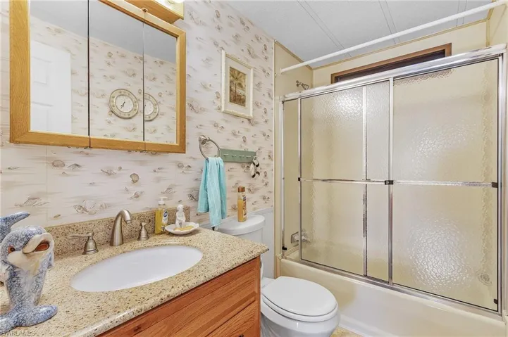 Full bathroom featuring bath / shower combo with glass door, toilet, vanity, and a textured ceiling