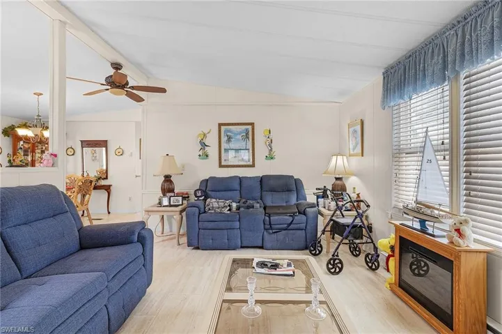 Living room featuring ceiling fan with notable chandelier, light hardwood / wood-style flooring, and vaulted ceiling