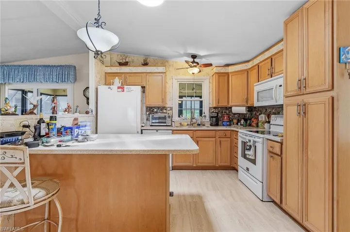 Kitchen with light hardwood / wood-style flooring, tasteful backsplash, white appliances, vaulted ceiling, and ceiling fan