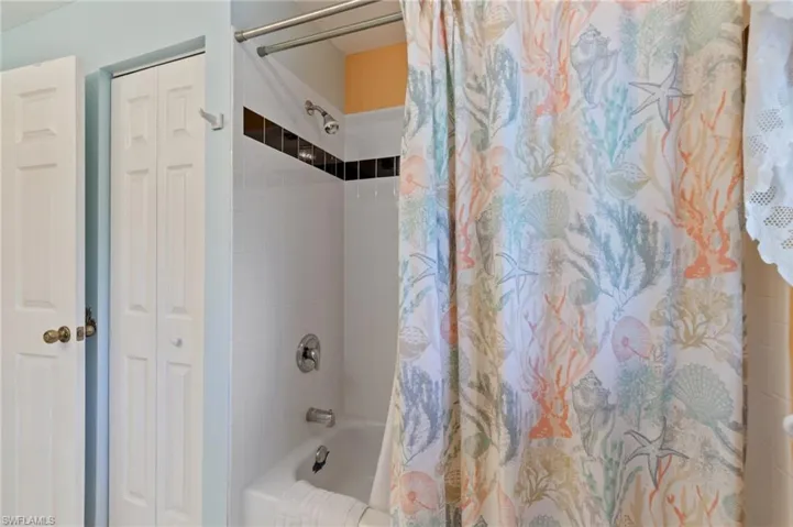 Bathroom with a closet and shower / bath combination with curtain