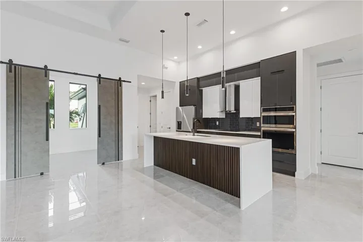 Kitchen with appliances with stainless steel finishes, a barn door, pendant lighting, a center island with sink, and wall chimney range hood