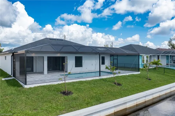 Back of house featuring screened enclosure, a lawn, a pool, and a patio