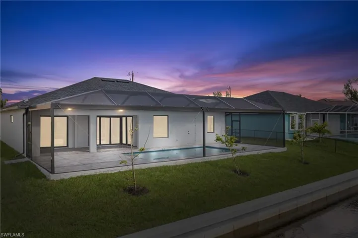 Back house at dusk featuring screened enclosure, a patio area, and a yard