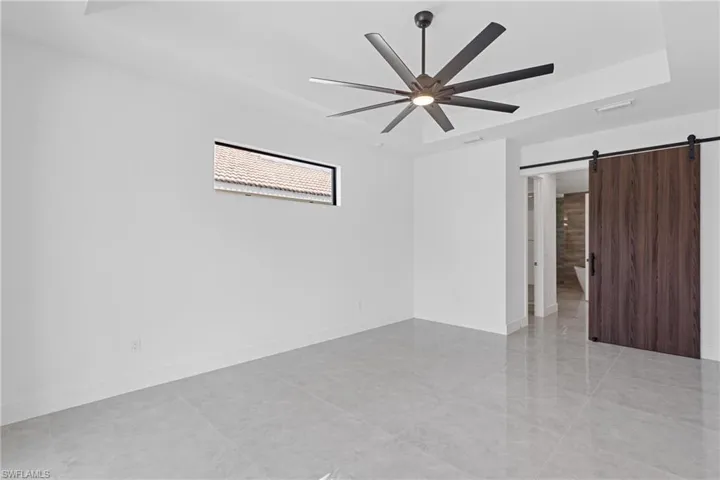 Empty room featuring ceiling fan, a raised ceiling, and a barn door