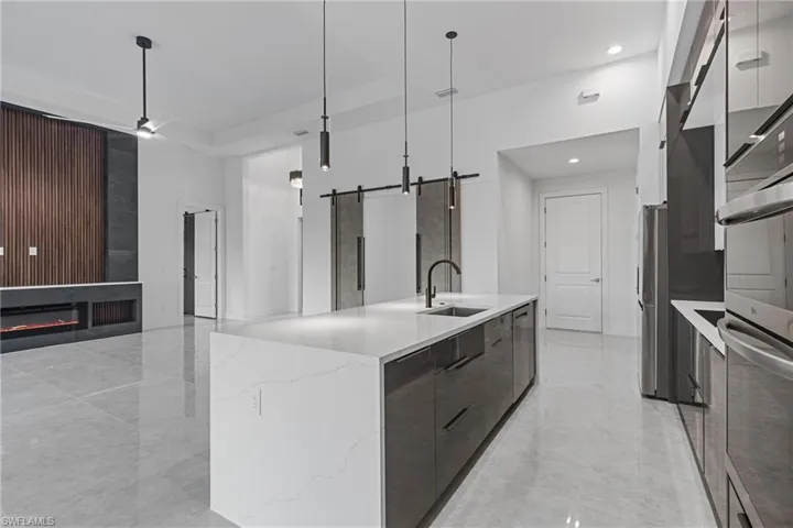 Kitchen featuring a barn door, a large island with sink, sink, and decorative light fixtures