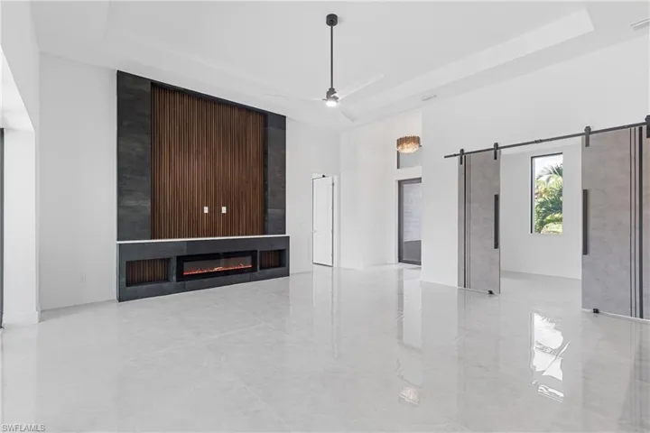 Unfurnished living room featuring ceiling fan, a raised ceiling, a fireplace, a towering ceiling, and a barn door