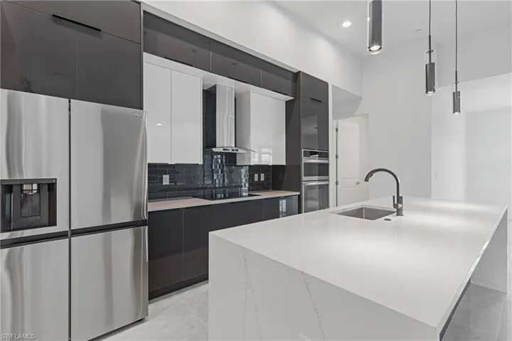 Kitchen featuring appliances with stainless steel finishes, pendant lighting, a center island with sink, sink, and wall chimney range hood