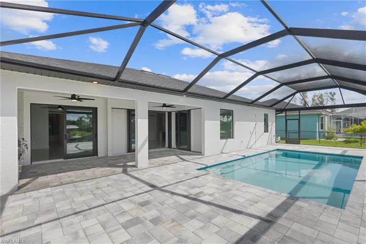 View of pool with ceiling fan, screened enclosure, and a patio area
