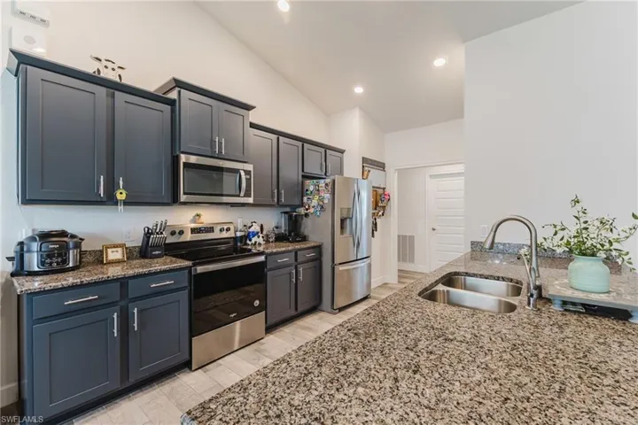 Kitchen featuring appliances with stainless steel finishes, dark stone countertops, lofted ceiling, light wood-style floors, and recessed lighting