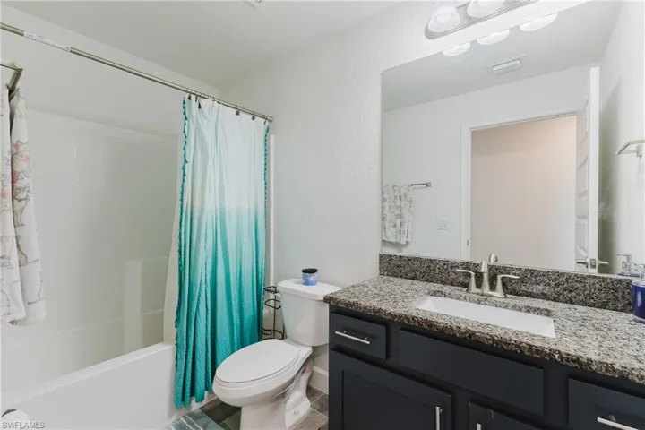 Full bathroom featuring shower / tub combo with curtain, vanity, and a textured wall
