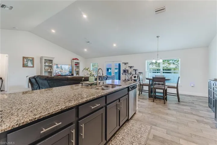 Kitchen featuring light stone countertops, open floor plan, light wood-type flooring, lofted ceiling, and recessed lighting