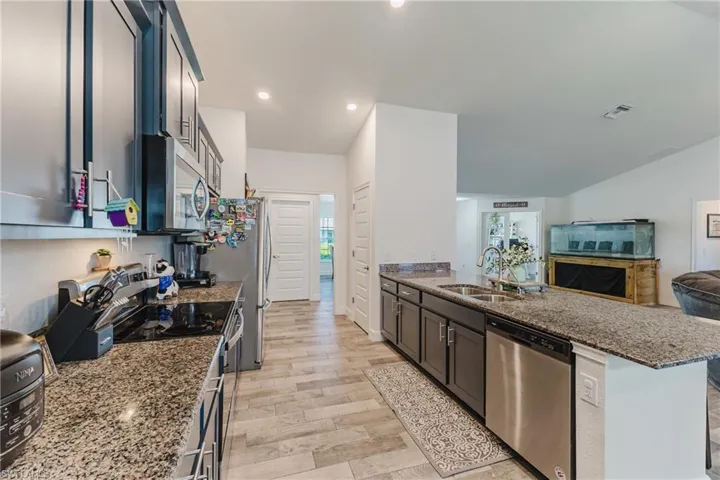 Kitchen featuring dark stone counters, appliances with stainless steel finishes, open floor plan, a peninsula, and recessed lighting