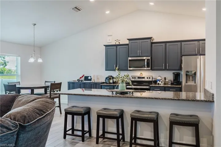 Kitchen featuring appliances with stainless steel finishes, a kitchen bar, light wood-style floors, pendant lighting, and high vaulted ceiling