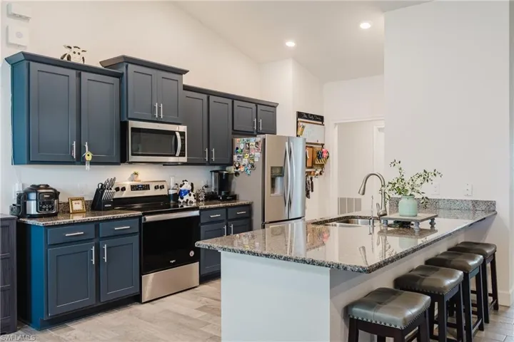 Kitchen featuring stainless steel appliances, dark stone countertops, light wood-style floors, a kitchen breakfast bar, and a peninsula