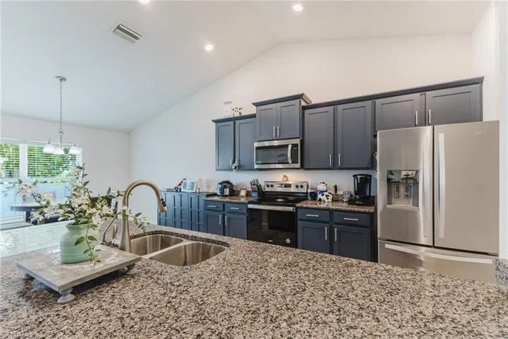 Kitchen featuring appliances with stainless steel finishes, light stone counters, pendant lighting, and high vaulted ceiling