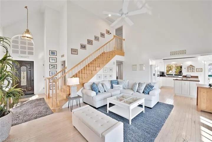 Living room with ceiling fan, high vaulted ceiling, and light hardwood / wood-style flooring