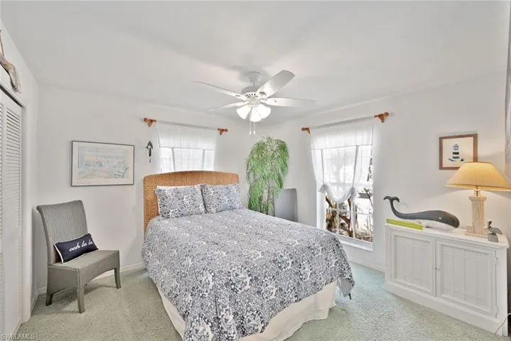 Bedroom with a closet, light colored carpet, multiple windows, and ceiling fan