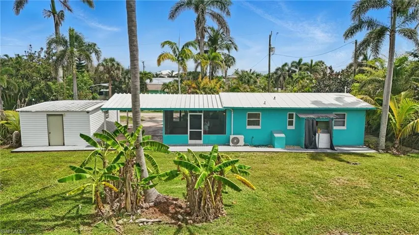 Back of property featuring a sunroom, a lawn, a metal roof, and a shed