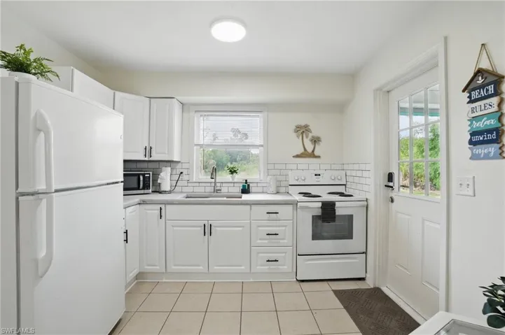 Kitchen featuring white appliances, light tile patterned flooring, decorative backsplash, light countertops, and white cabinets
