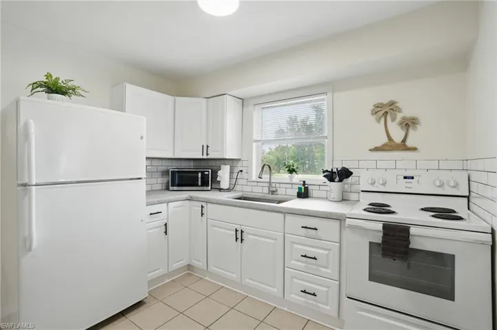 Kitchen featuring white appliances, light tile patterned flooring, backsplash, and light countertops
