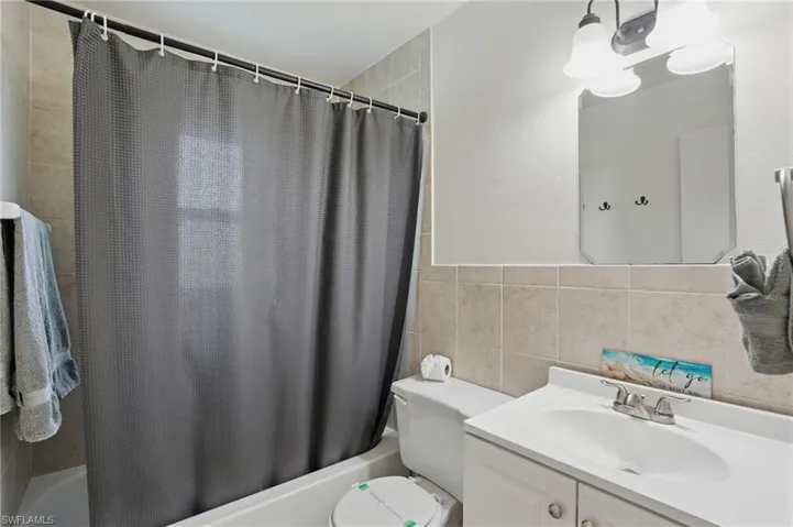Bathroom featuring shower / bath combo, vanity, and tile walls