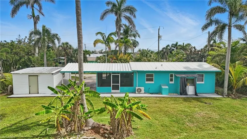 Rear view of property featuring a sunroom, a yard, a metal roof, and a shed