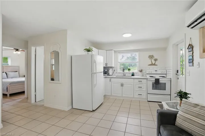 Kitchen featuring white appliances, light tile patterned floors, a wall mounted air conditioner, backsplash, and light countertops