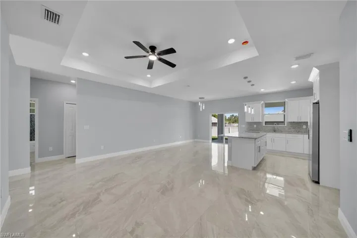 Unfurnished living room with a ceiling fan, a tray ceiling, a sink, recessed lighting, and baseboards
