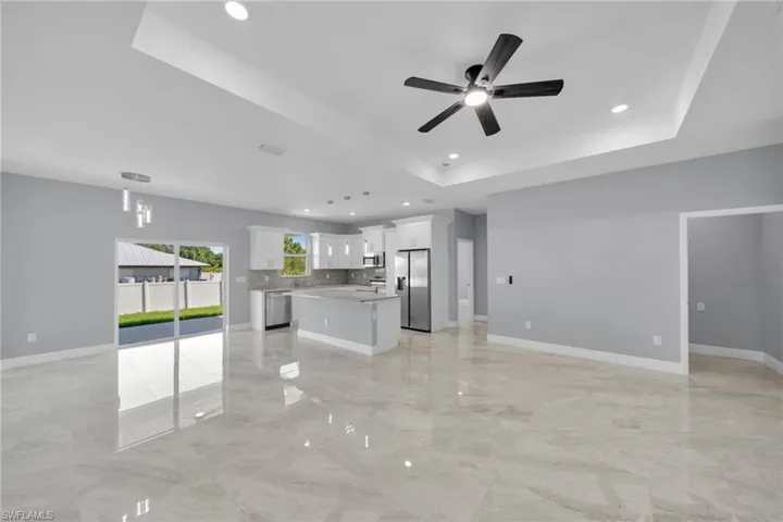 Unfurnished living room featuring recessed lighting, a tray ceiling, a ceiling fan, light marble finish floors, and baseboards