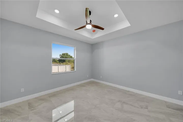 Empty room with a raised ceiling, ceiling fan, baseboards, and recessed lighting