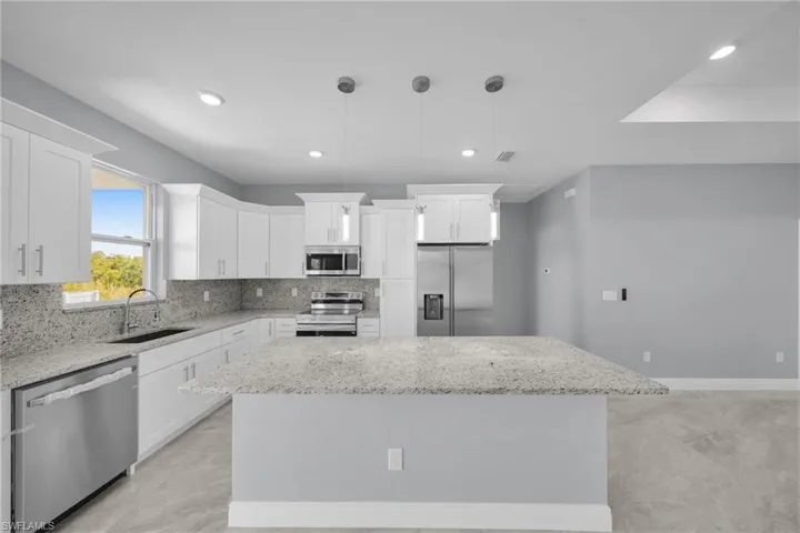 Kitchen featuring appliances with stainless steel finishes, a sink, a center island, white cabinetry, and light stone counters