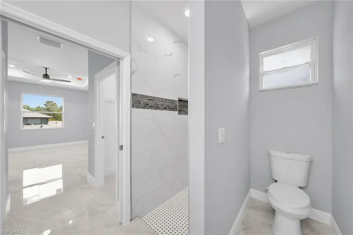 Bathroom featuring a marble finish shower, marble finish floors, toilet, baseboards, and a ceiling fan