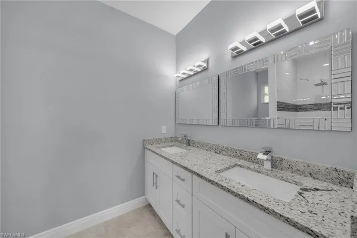 Bathroom with double vanity, baseboards, walk in shower, and marble look tile flooring