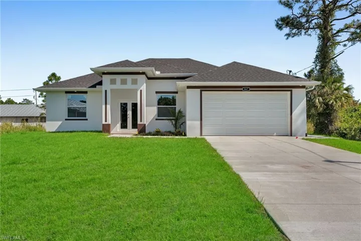 Prairie-style house with stucco siding, a front lawn, french doors, concrete driveway, and an attached garage