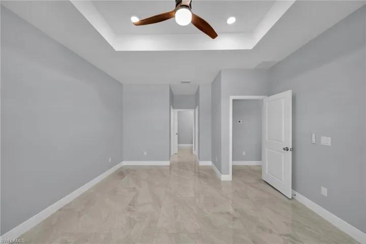 Unfurnished room with a ceiling fan, a tray ceiling, and baseboards