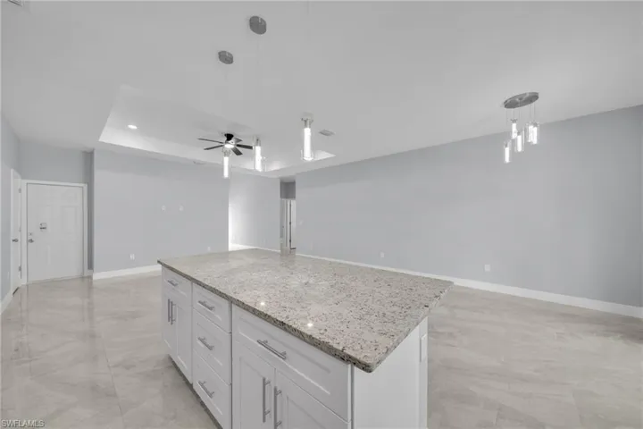 Kitchen with open floor plan, a kitchen island, hanging light fixtures, white cabinets, and light marble finish flooring