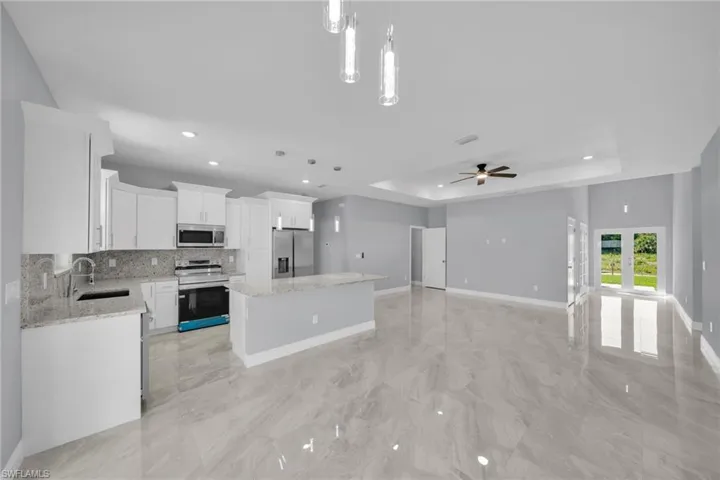 Kitchen with stainless steel appliances, a tray ceiling, a kitchen island, decorative backsplash, and a sink