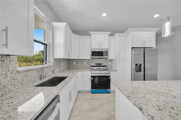 Kitchen with stainless steel appliances, a sink, white cabinets, light stone countertops, and recessed lighting