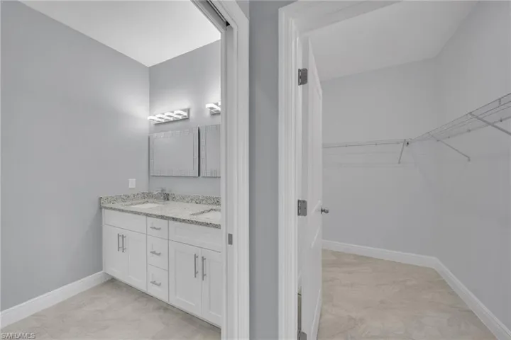 Bathroom with double vanity, baseboards, a walk in closet, and marble finish floors