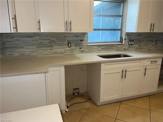 Kitchen featuring white cabinetry, sink, tasteful backsplash, and light tile patterned floors