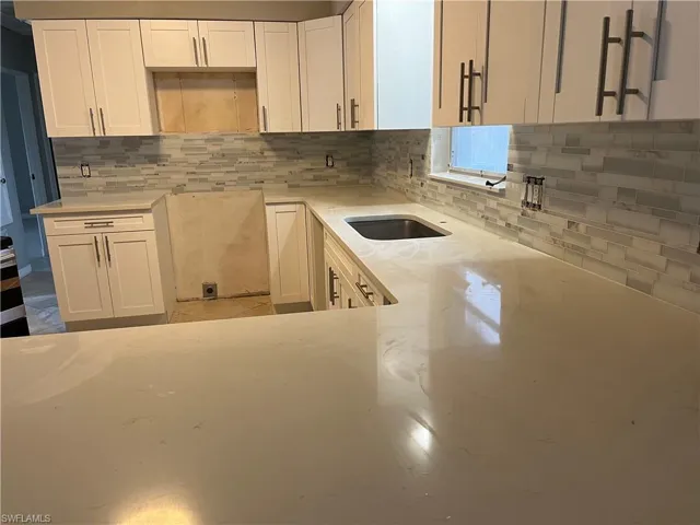 Kitchen featuring white cabinetry, light stone countertops, and backsplash