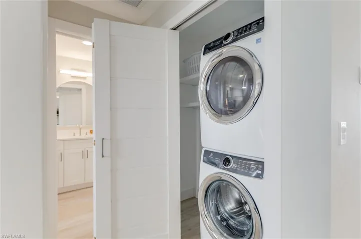 Washroom with stacked washer / drying machine and light wood-style flooring