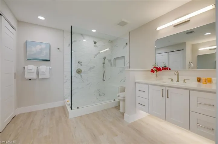 Bathroom featuring vanity, light wood-style flooring, a marble finish shower, and recessed lighting
