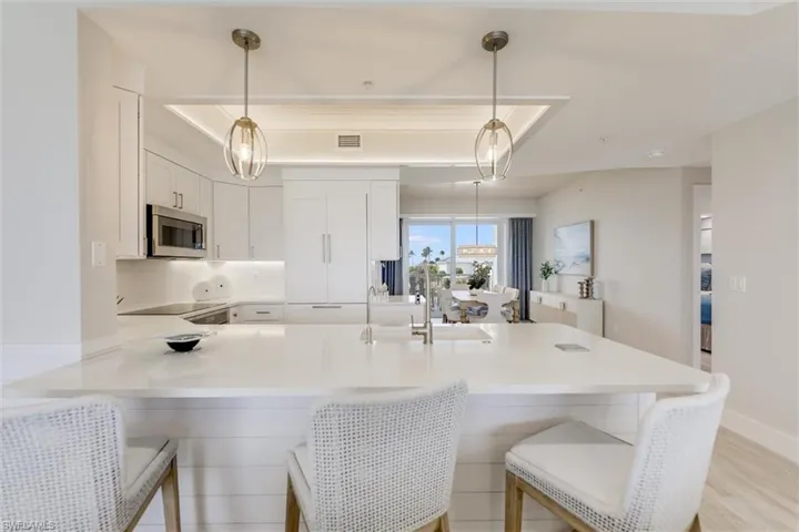 Kitchen featuring decorative light fixtures, white cabinets, a breakfast bar, and a peninsula