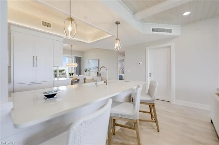Kitchen with a breakfast bar area, white cabinetry, light wood-style flooring, hanging light fixtures, and a wooden ceiling with exposed beams