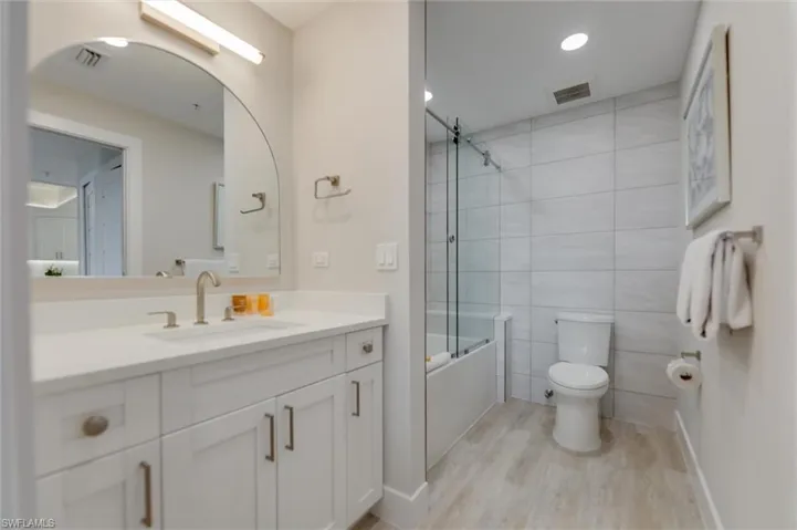 Full bathroom featuring vanity, shower / bath combination with glass door, light wood-style flooring, tile walls, and recessed lighting