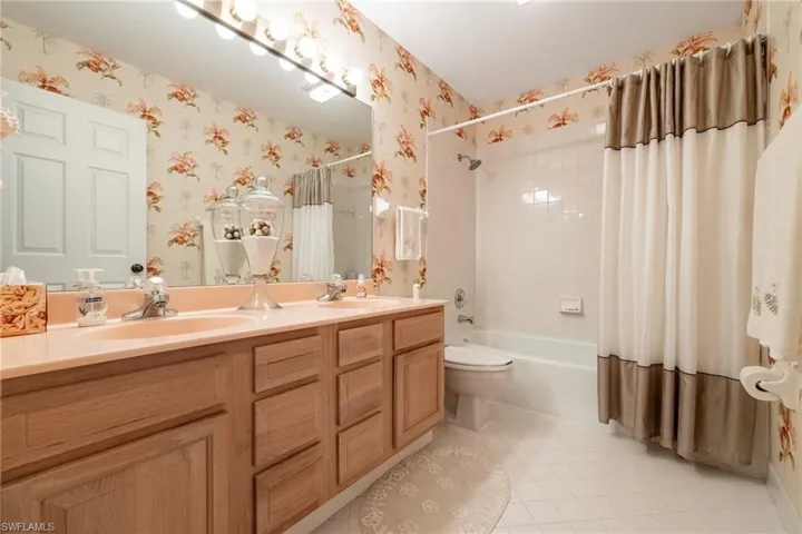 Full bathroom featuring double vanity, shower / tub combo, light tile patterned flooring, and wallpapered walls